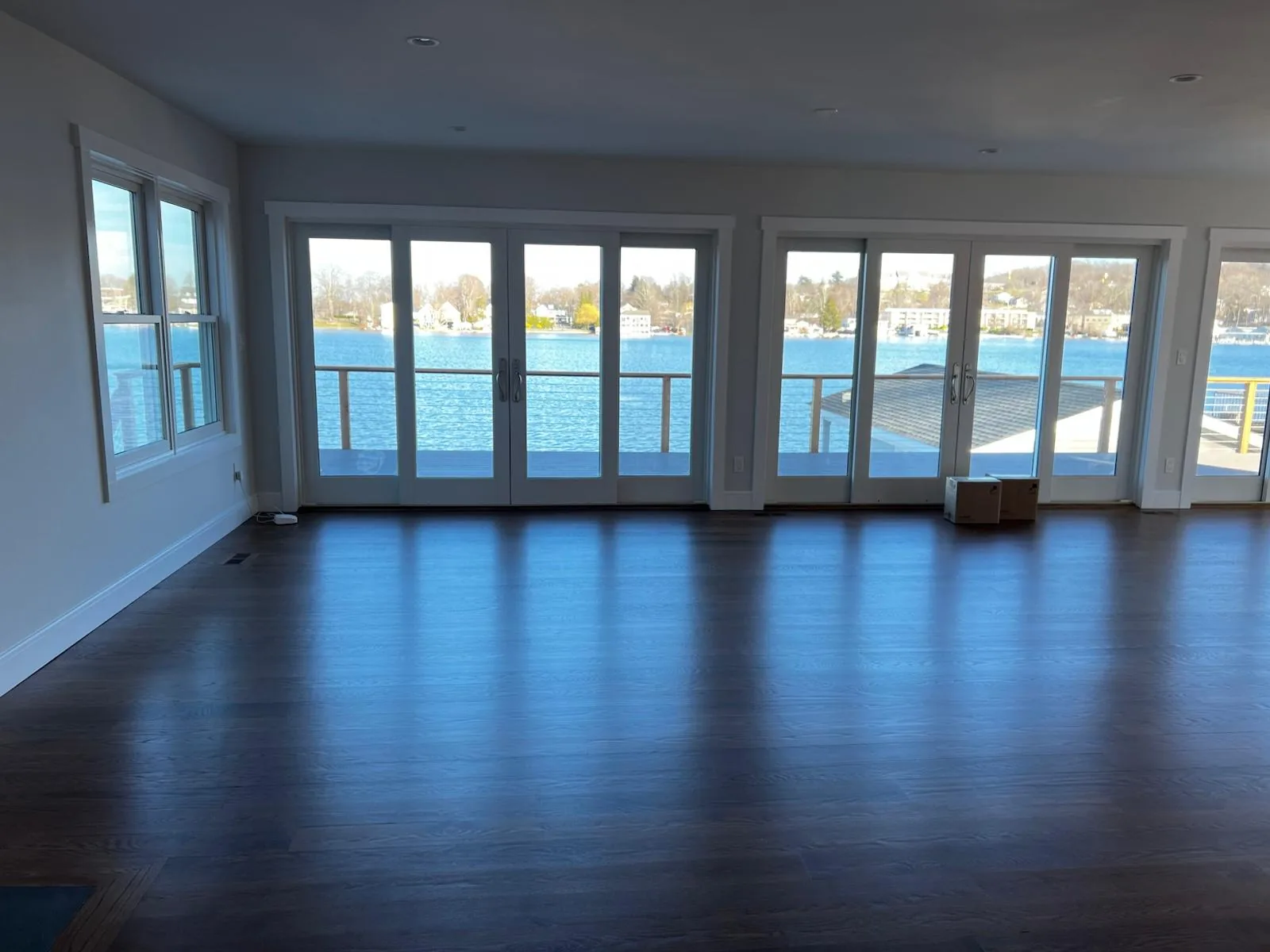 Empty living room with clean wood floors and glass doors facing a lake