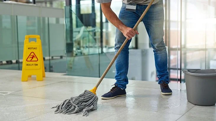 Mopping a tile floor beside a wet-floor sign